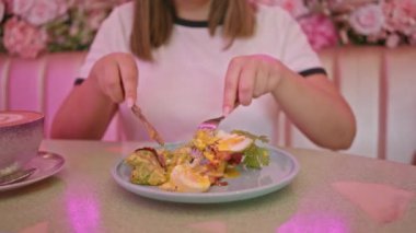 Neon ışıkları ve çiçek dekoru olan pembe kafede yemek yiyen bir kadın.