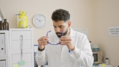 Sakallı bir adam, güvenlik gözlüklerini profesyonelliği ve sağlık hizmetlerini temsil eden bir laboratuvar ortamında ayarlar..