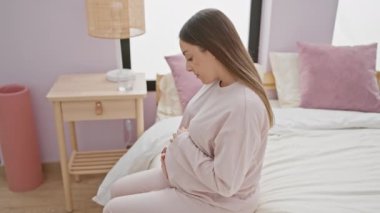 Huzurlu hamile bir kadın, rahat bir yatak odasında, derin derin yatakta oturur, anne beklentisinin somutlaştırıcısıdır..