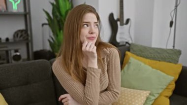 Gergin, genç, sarışın bir kadın, elleri çenesinde, süveter giyiyor, son derece endişeli ve endişeli, evinde rahatsız edici bir soruyu düşünüyor..