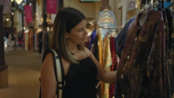 一位面带微笑的年轻女子在杜拜州朱美拉市朝气蓬勃的马迪纳河畔商店里买传统服装 — 图库视频影像