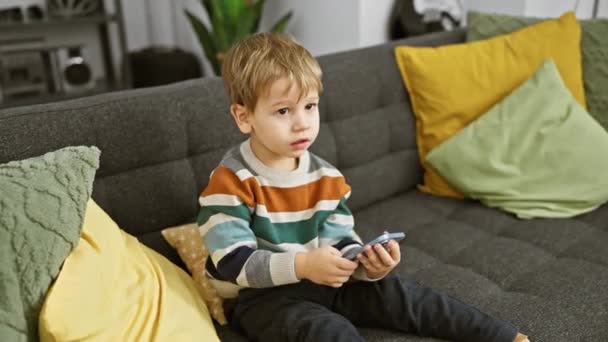 スマートフォンを持っている灰色のソファに焦点を当てた子供が居心地の良いリビングルームで座ります — ストック動画