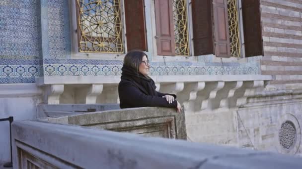 イスタンブールのトップカピ宮殿のバルコニーに傾いているスカーフの笑顔の女性は 伝統的な建築を示しています — ストック動画