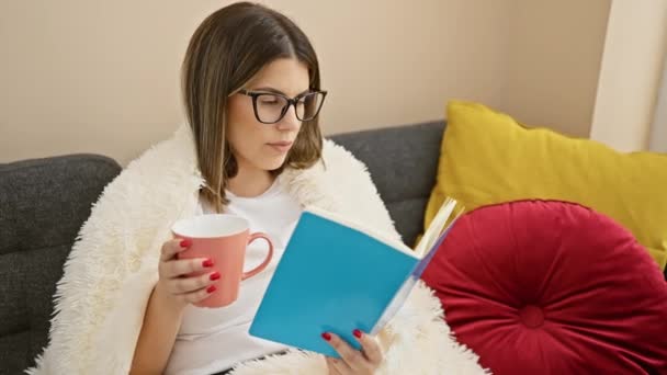一个年轻的惊慌失措的女人在舒适的客厅里拿着一本书和一个杯子放松下来 — 图库视频影像