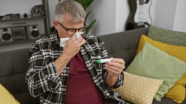 Grey Haired Man Checks Thermometer While Blowing Nose Sitting Couch — Stock Video