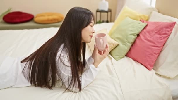 Rahatlamış Asyalı Bir Kadın Yatakta Sıcak Bir Içkiden Hoşlanır Aydınlatılmış — Stok video