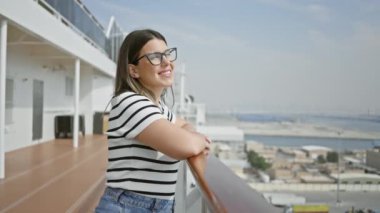 Gözlüklü gülümseyen kadın bulanık deniz ve şehir manzarasına karşı yolcu güvertesinde eğleniyor..