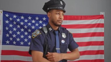 Kapalı alanda ABD bayrağı önünde kollarını kavuşturup otoriteyi ve gururu tasvir eden Afro-Amerikan polis memuru..