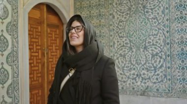 Gözlüklü ve eşarplı gülümseyen bir kadın İstanbul 'un tarihi Topkapı sarayının içini keşfediyor..