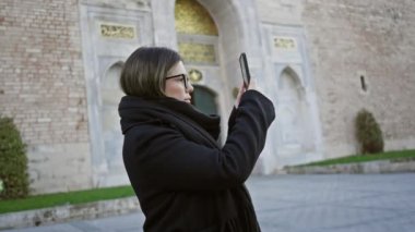 Gözlüklü esmer bir kadın İstanbul 'daki Topkapı Sarayı' nda akıllı telefon kullanıyor. Seyahat ve tarih çağrıştırıyor..
