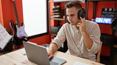 Kulaklıklı bir adam canlı bir kayıt stüdyosundaki laptopta ses düzenliyor..