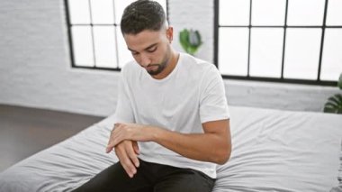 Yakışıklı bir genç, modern bir yatak odası ortamında kollarına losyon sürüyor..