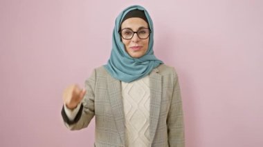 Kendine güvenen orta yaşlı tesettürlü İspanyol kadın parmaklarıyla küçük boy işareti yapıyor, izole edilmiş pembe arka plan üzerindeki ölçü kavramını gösteriyor.
