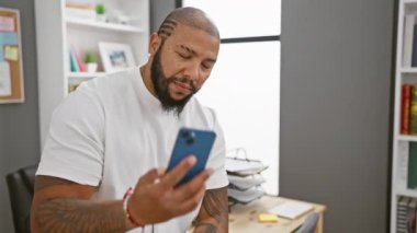 Gülümseyen Afro-Amerikan sakallı adam modern ofis ortamında telefonla konuşuyor.