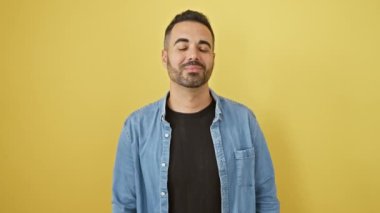 Kot gömlekli neşeli, genç İspanyol bir adam, 'buraya gel' işareti yapıyor, mutlu bir davetiye dolu, izole edilmiş sarı bir arka plana karşı duruyor..