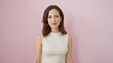 Neşeli, genç İspanyol kadın parmaklarının arasından gözetleyerek eğlenceli bir el hareketi yapıyor. Ayakta, rahat kolsuz bir tişört giyerek, canlı, izole pembe bir arka plana karşı..