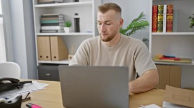 Modern ofiste dizüstü bilgisayar ve masa başında telefonla konuşurken sakallı beyaz bir adam gülümsüyor.