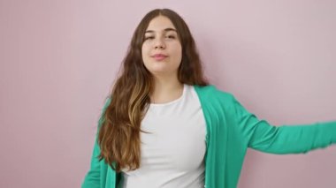 Mutlu, genç, İspanyol bir kadın, neşeli bir şekilde burnunu işaret ediyor. Güzel bir gülümseme, berrak, sağlıklı cildinin üzerinde açıyor. Pembe bir arka plana izole edilmiş, doğal güzelliği kucaklıyor. 