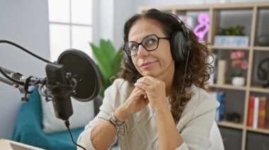 Heyecanlı orta yaşlı İspanyol bir kadın, kendine güvenen bir radyo stüdyosu yıldızı, bir parmağını havaya kaldırıyor, kulaklıklarının altındaki mutlu yüzüne bir 