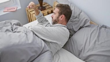 Pijamalı bir adam, çağdaş bir yatak odasında sabah uyanma rutinini canlandırarak yatakta esniyor..