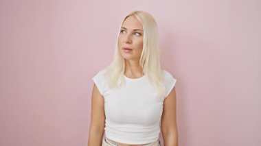 Şişt! Güzel sarışın kadın sırrı saklar, sessiz bir şekilde işaret eder, parmakları dudaklarında, pembe, izole bir arkaplanda durur..