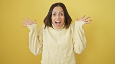 Heyecanlı genç İspanyol kadın, zaferini sevinçle kutluyor. Sarı arka planda bir süveter giyiyordu. Kolları muzaffer bir şekilde kaldırılmıştı. Mutlu kazanan başarıyı ifade eder.!