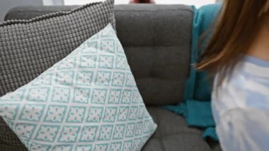 Rahat genç bir kadın rahat bir evde akıllı telefonunu kullanarak bir kanepeye uzanır..
