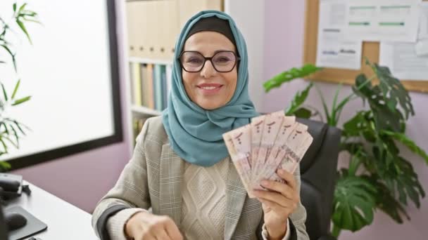 陽気な中年ヒジャブのヒスパニック女性 リヤルを保持し 優れたOkサインを点滅 輝く笑顔 オフィスでフレンドリーなバイブをオフ — ストック動画