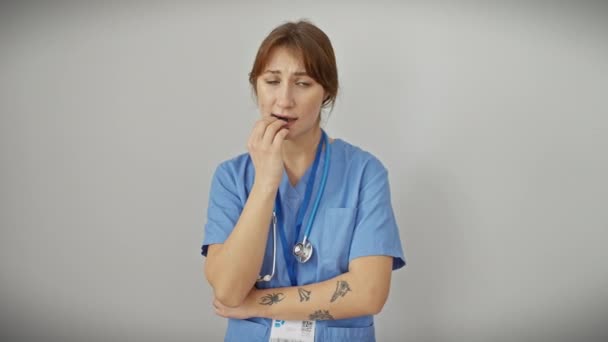 焦虑的年轻的高加索女人 穿着制服的医生咬指甲 表现出恐惧 戴听诊器 隔离在白色背景上 表现出焦虑问题 — 图库视频影像