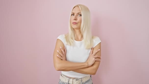 ピンクの背景の上に交差した腕で立っている若い金髪の女性は 顔の表情を不承認し 懐疑主義と否定を投影 — ストック動画