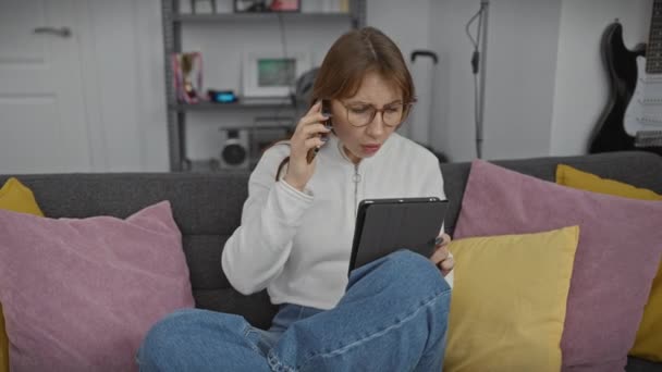 一个年轻女人在她的现代客厅里忙着多项任务 一边打电话一边用平板电脑 — 图库视频影像