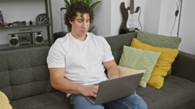 Heyecanlı genç İspanyol adam, evdeki kanepede otururken sevinçle dizüstü bilgisayarı gösteriyor, kendine güvenen gülümseme ve ışıl ışıl gözler umut verici bir fikri ortaya çıkarıyor..