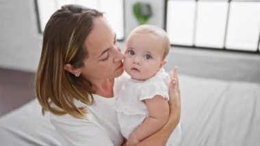 Neşeli bir annenin kızını kucaklaması ve öpmesi, rahat bir yatak odasında rahat ve eğlenceli bir anın tadını çıkarması, kendine güveni ve olumlu aile ilişkisini ifade etmesi..