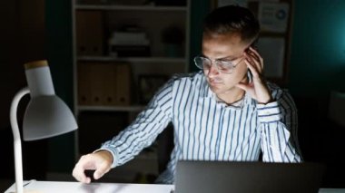 Karanlık ofis odasında dizüstü bilgisayarla çalışan odaklanmış genç bir adam.