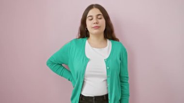 Genç ve güzel İspanyol bir kadın neşeli bir sürprizi gizliyor, bir elle gözlerini kapatıyor, pembe izole bir duvarın önünde duruyor, kendine güvenle dolup taşıyor, canlı sırrının üzerinde gülümsüyor.