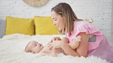 Mutlu anne yatakta oturuyor, gülüyor ve mutlu kızıyla rahat bir yatak odasında oynuyor, rahat bir yaşam tarzında güven ve sevgisini ifade ediyor.