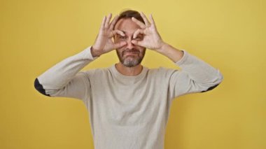 Neşeli orta yaşlı İspanyol adam, 'tamam' el hareketini izlerken dilini dışarı çıkartıyor, izole edilmiş sarı arka plana karşı duruyor, neşe ve neşe içinde ışıldıyor..
