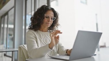 Ofisteki olgun İspanyol kadın dizüstü bilgisayardan heyecan ve neşeye kadar değişik duygular gösteriyor.