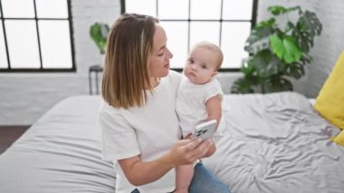 Sıcak yatak odasında, kendinden emin bir anne ve mutlu kızı birlikte biraz eğleniyorlar, yatakta oturmuş akıllı telefon ekranlarına bakıyorlar..