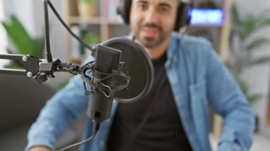 Modern bir radyo stüdyosunda mikrofona konuşan sakallı İspanyol bir adam.