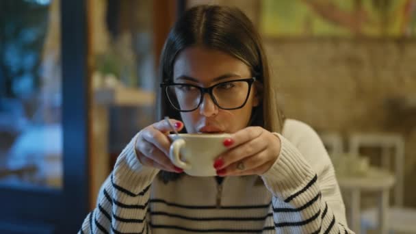 여성은 아늑한 카페에서 커피를 마시며 우아한 안경과 매니큐어 손톱으로 편안한 — 비디오