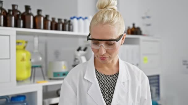 年轻快乐的金发女科学家 信心十足 戴着安全眼镜微笑着 在一个繁华的实验室里探索科学之美 — 图库视频影像