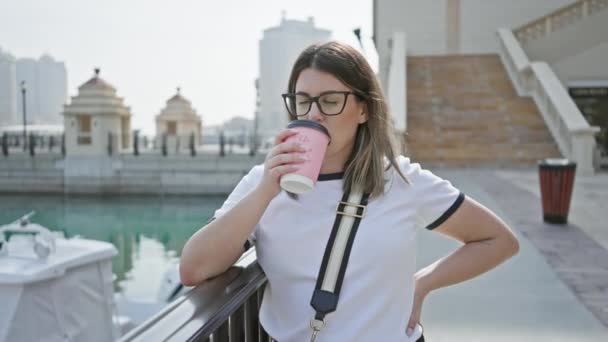 一位年轻的黑发女子在现代的码头边喝咖啡 展示了她的旅行和生活方式 — 图库视频影像