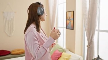 Genç bir kadın, rahat bir yatak odasında kulaklıklarla müzik dinlemeyi sever..