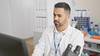 Genç, stresli, bilim adamı üniformalı, migren ağrısı çeken, laboratuarda bilgisayar başında çalışan bir İspanyol.