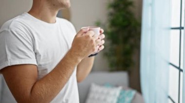 Düşünceli bir genç adam, sıcak bir odada kahve fincanıyla huzurlu bir anın tadını çıkarıyor..