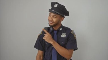 Polis üniforması giymiş neşeli Afro-Amerikalı adam, büyük bir gülümseme gösterip, izole edilmiş beyaz bir arka planda işaret ediyor.