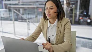 İş yerindeki stresli genç İspanyol kadın bulanık bir ofis geçmişine karşı kulaklıklarını çıkarıyor.