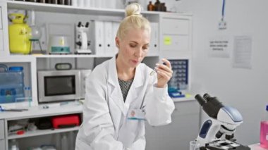 Bilim dünyasına ilgi çekici bir bakış, güzel sarışın bilim adamı titizlikle deney gözlemlerini not ederken tıbbi olarak gelişmiş bir laboratuvarda bir deney tüpüne bakıyor..