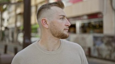 Şehir ortamında sakallı yakışıklı genç bir adam, şehirde güvenle gülümsüyor..